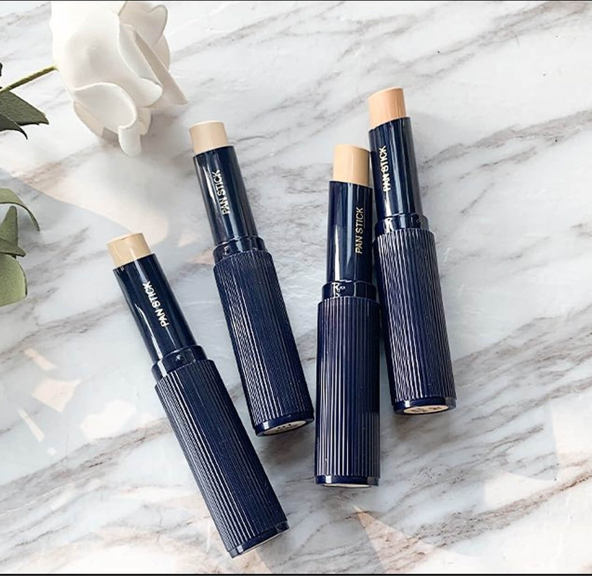 Five makeup sticks with visible brand name on a marble surface
