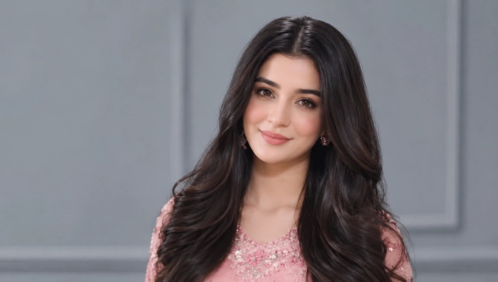 Woman with long dark hair wearing a pink dress against a gray background