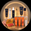 Cosmetic products including lip palette, bottles, and tubes on a reflective surface with a glowing circular background.